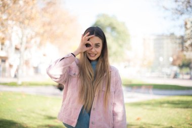 Genç, güzel, sarışın, pembe ceketli bir kadın parkta iyi görünüyor.  
