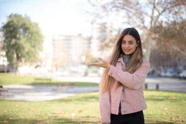 Pembe ceketli güzel sarışın kadın parkta bir şey gösteriyor.  