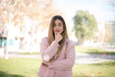 Genç, güzel, sarışın, pembe ceketli bir kadın parkta düşünüyor.  