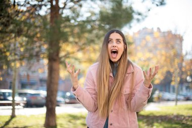 Genç, güzel, sarışın, pembe ceketli kadın parkta bağırıyor.  