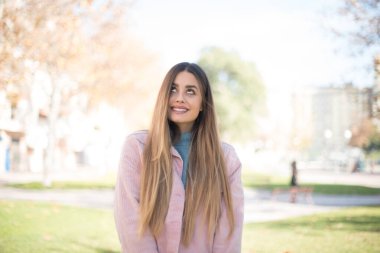 Genç, güzel, sarışın, pembe ceketli bir kadın parka bakıyor.  