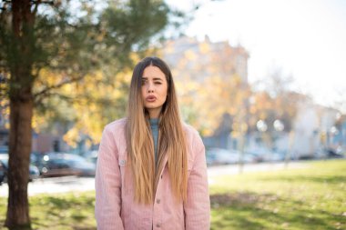 Pembe ceketli güzel sarışın kadın parkta göz kırpıyor.  