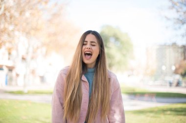 Genç, güzel, sarışın, pembe ceketli kadın parkta bağırıyor.  