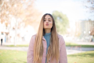 Genç, güzel, sarışın, pembe ceketli, parkta öpüşen bir kadın.  