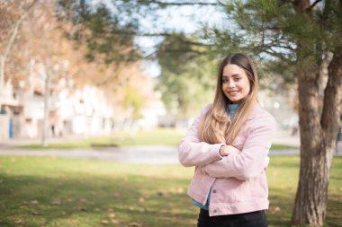 Kolları açık havada duran neşeli, yeşil gözlü genç bir kadının portresi. Güzel beyaz kız kollarını kavuşturup kameraya bakıp gülümsüyor.
