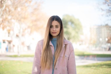 Güven ve iş kavramı. Pembe ceketli, kendine güvenen bir ifadeyle gülümseyen çekici sarışın kadın portresi.