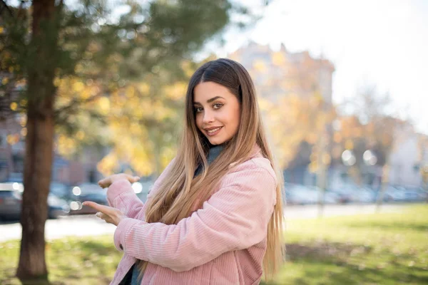 Pembe ceketli güzel sarışın kadın parkta bir şey gösteriyor.  