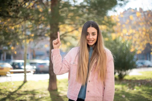 Olumlu ve çekici genç bir kadın, ağzı açık neşeli ve gülümseyen bir yüz ifadesiyle açık havada inanılmaz bir şey gösteriyor. Reklam kavramı.