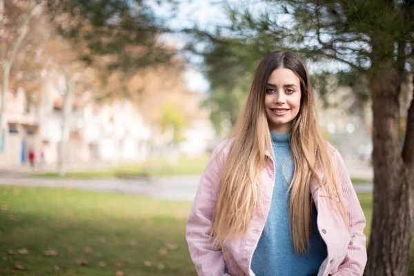 Neşeli, çekici sarışın kız ellerini aşağıda tutuyor ve gülümsüyor ve kendinden emin, günlük kıyafetler giyiyor ve güçlü bir görünüm sergiliyor. Mutlu genç kadın.