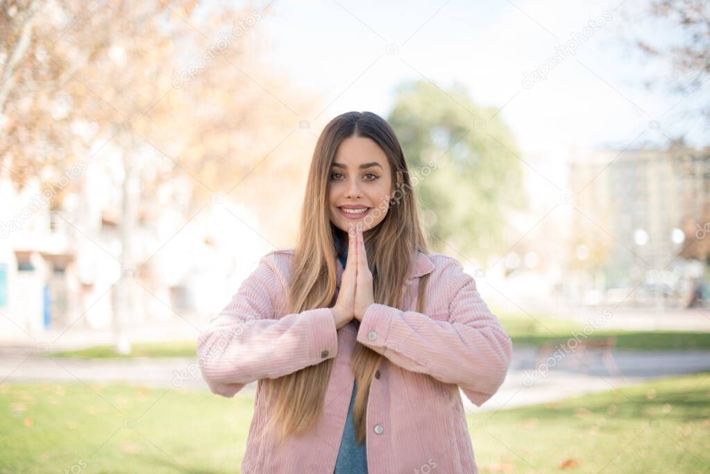 young beautiful blonde woman wearing pink jacket is showing pleased gesture in the park  