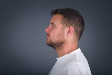 Sağlıklı ve saf cilde sahip gülümseyen bir adamın profili gür saç stiline sahip, derin düşüncelere dalmış, dışarıda yürümeye hazır, beyaz stüdyo duvarının üzerinde fotokopi alanı ile izole edilmiş.