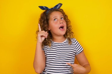 Sarı arka planda kıvırcık saçlı beyaz kız parmağıyla işaret ediyor. 