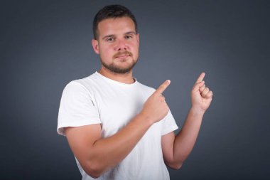 Olumlu ifadeli hoş bir genç adam, gelişigüzel giyinmiş, tanıtım metnin ya da reklamın için boş fotokopi yerindeki parmaklarıyla gösteriyor. Sevimli adam evde tek başına poz veriyor.