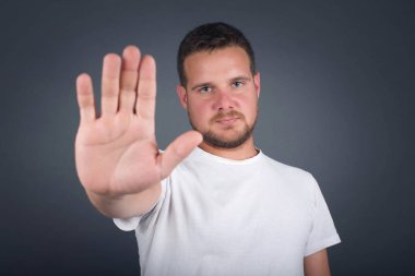 Genç, yakışıklı, beyaz bir adam avucunun içinde el hareketi yapıyor. Gri arkaplan üzerinde izole edilmiş yüz üzerinde negatif ve ciddi jest içeren uyarı ifadesi.