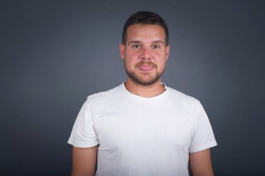 Gülümseyen ve dil gösteren mutlu ve komik yüzlü güzel beyaz bir adam. Günlük giysiler giyip gri stüdyonun arka planında dikiliyorlar..