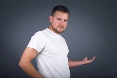 Gri arka planda hoş geldin jesti yapan kolları açık yakışıklı genç adamın portresi..