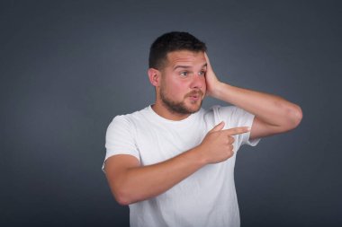 Positive glad  man  says: wow how exciting it is, has amazed expression, indicates something. Joyful pretty young man demonstrates something. One hand on her head and pointing with other hand.