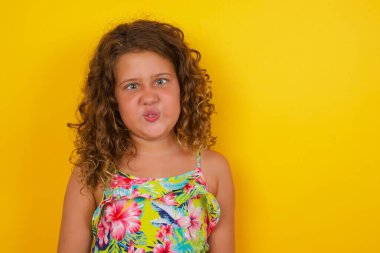 Sarı arka planda yazlık elbise giyen komik küçük kız gözlerini şaşı yapar, dudaklarını büzer, bütün gün çalıştıktan sonra suratını buruşturur. Tuhaf ifadeli cahil kız ineği. Yalnız eğleniyor, aptalı oynuyor..