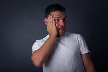 Şaşkınlık - adam heyecanla yüzüne bakıyor. Heyecandan yana bakan mutlu genç adam şaşırdı. Gri arka planda beyaz erkek model.   