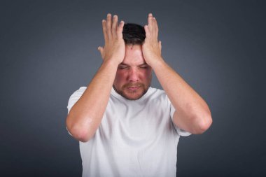 Sinir bozucu bir adam ellerini şakaklara koyar, baş ağrısı hisseder, acıdan gözleri kapar, sağlıklı bir uykuya ihtiyacı vardır, aşırı çalışma, yorgunluk ve yorgunluk. Avrupalı adam hasta, gri arka planda izole.