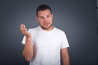 What the hell are you talking about, nonsense. Studio shot of frustrated male with blond hair gesturing with raised palm, frowning, being displeased and confused with dumb question over gray wall.