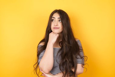 Düşünceli kadın portresi elini çenesinin altında tutuyor, bir şey hatırlamaya çalışıyor ya da ilgi çekici bir şey dinliyor, sıradan giyiniyor, içeride poz veriyor. Gençlik kavramı.