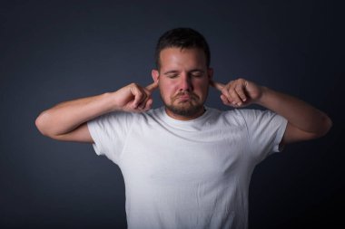 Bu sinir bozucu sesi çıkarmayı kes! Mutsuz genç adamın endişeli yüz ifadeleri, parmaklarıyla kulakları tıkayan, üst katındaki komşulardan gelen gürültüden rahatsız olmuş bir portre..