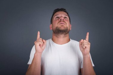 Olumlu ifadeli, kaygısız, her iki işaret parmağıyla işaret eden, günlük kıyafetler giymiş, pembe arka planda soyutlanmış, geniş bir tebessüme sahip, tasasız bir adam. Şuraya bakın, lütfen. 