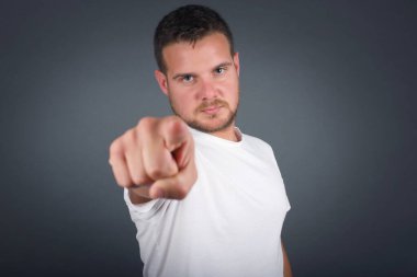 Kapalı mekandaki günlük giysiler içindeki neşeli genç adam fotoğrafı size mutluluğu gösteriyor, rekabeti seçiyor, olumlu bir ifadeye sahip. Yakışıklı zeki öğrenci, gri duvarda izole edilmiş bir şekilde seçim yapar.