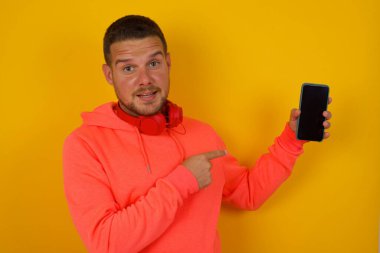 Genç yakışıklı adam akıllı telefonu sarı duvara doğrultuyor 