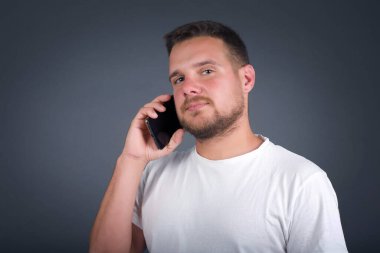 Gündelik giysiler içindeki çekici genç adam telefon konuşmasını taklit ediyor, cep telefonu tutar gibi elini kulağına yaklaştırıyor, kendine güvenen bir yüz ifadesi var, dışarıda izole edilmiş. Ara beni.!