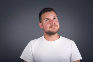 Esrarengiz bir gülümseme ile yukarı bakan düz saçlı gizemli çekici bir adamın portresi. Yakışıklı, gülümseyen adam gri duvara bakıyor..