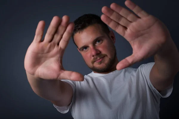 Gesturing finger frame. Portrait of smiling handsome young man looking at camera and gesturing finger frame while standing against gray studio wall.