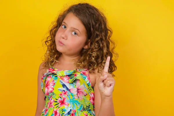 小女孩穿着黄色背景的夏装 给人一种注意的感觉 一个严肃的女孩举起手指 — 图库照片