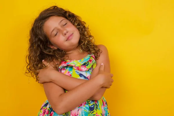 在黄色背景下穿着夏装 抱着自己的漂亮而平静的小女孩的画像 — 图库照片