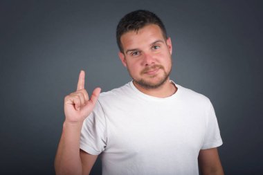 Hoş görünümlü mavi gözlü genç adam modelinin yakın portresi zekice bir ifadeye sahiptir, bir parmağını kaldırır, önemli bir şeyi unutmaması gerektiğini hatırlar..