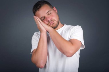 Rahatla ve uyu. Avuç içlerine yaslanmış, yorgun, genç ve yakışıklı bir adam. Yastık gibi uzanmış, yorgun düşmüş gibi yapıyor. Gri arka planda duran rüyalar görüyor. Uyuma hareketi.