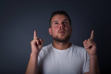 Yakışıklı, zarif bir adamın portresi izole edilmiş arka planda şaşkın şaşkın bakıyor ve parmaklarıyla garip bir şey gösteriyor..