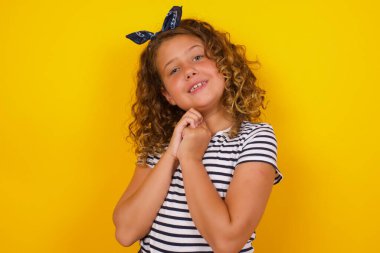 Hoş bir yüz ifadesi olan rüya gibi çekici bir kız, ellerini yüzüne çarpıyor, hoş bir şey için heyecanlı, arka planda poz veriyor..