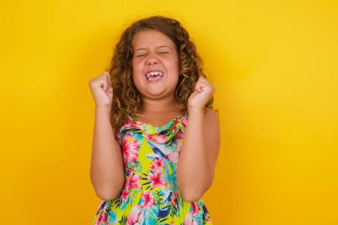 Sarı arka plan birincisinin üzerine yaz elbisesi giymiş güçlü, kararlı genç kızın belden yukarı portresi, neşe ve heyecanla haykırıyor. Zafer, başarı ve başarı kavramı.