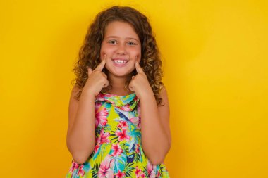 Güçlü, sağlıklı, beyaz dişlere sahip olma kavramı. Sarı arka planda, kusursuz beyaz dişleri olan, küçük mutlu bir kızın, yaz elbisesi giymiş portresini kapat.