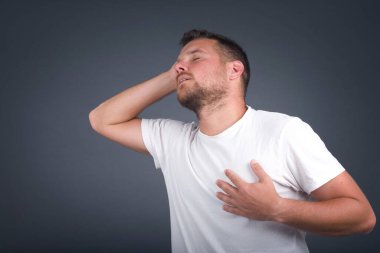 Neşeli Avrupalı bir adam iyi bir şakaya gülüyor ve eğleniyor ya da günlük kıyafetler giyiyor, gri duvara yaslanıyor.