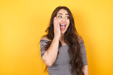 Şaşırmış heyecanlı kadın, elinde yüzüyle yan tarafa bakıyor. Heyecandan yana bakan mutlu genç bir kadın. Beyaz kadın model, uzun siyah saçlı.