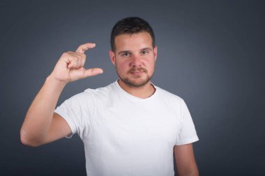 Sarışın Avrupalı bir adam, izole edilmiş arka planda, küçük boy ve ölçü sembolü gösteren el hareketleriyle. Kameraya bakıp gülümsüyor. Ölçüm konsepti.