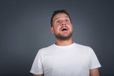 İnsanlar ve ani tepki kavramı. Şaşırmış beyaz, yakışıklı erkek öğrenci, omuz silkiyor, yana bakıyor, arkadaşlarıyla yeni planları için mutlu ve heyecanlı. Gri duvarda izole edilmiş..