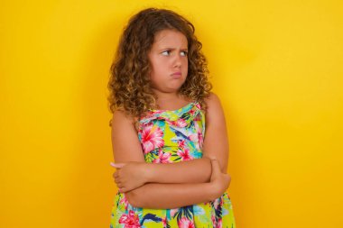 Sarı arka planda yazlık elbise giyen üzgün, genç ve güzel bir kızın görüntüsü. Kapalı alanda kollarını kavuşturmuş duruyor. Hayal kırıklığına uğradım. 