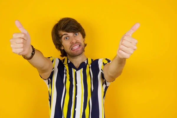 Good job! Portrait of a happy smiling blue eyed young successful man giving two thumbs up gesture standing indoors. Positive human emotion facial expression body language. Funny girl