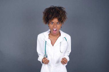 Tıbbi üniforma giyen, kollarını kaldıran, yumruklarını sıkan, hedeflerini sevinç ve heyecanla haykıran Afrikalı Amerikalı doktor kadın portresi. Zafer, başarı ve başarı kavramı.