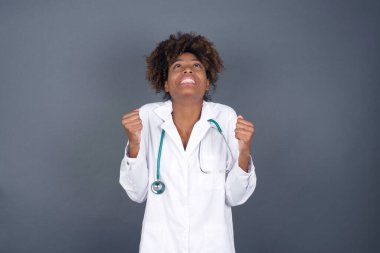 Heyecanlı, Afro-Amerikan doktor üniformalı kadın, maçı kazandıktan sonra keyifli bir şekilde yumruklarını kaldırıyor. Genç şampiyon hedeflerine ulaştığına seviniyor. Zafer ve zafer kavramı.