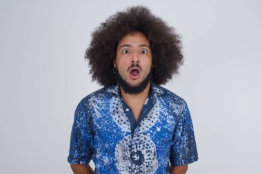 Ağzı açık duygusal çekici bir adam büyük bir şaşkınlık ve korku ifade ediyor, beyaz beton arka plana karşı duruyor, kameraya bakıyor. Beklenmedik haberler ve insani tepkiler.